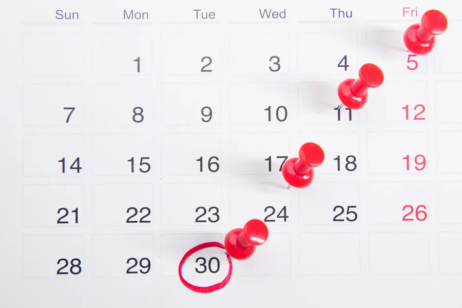 A calendar with red push pins marking dates