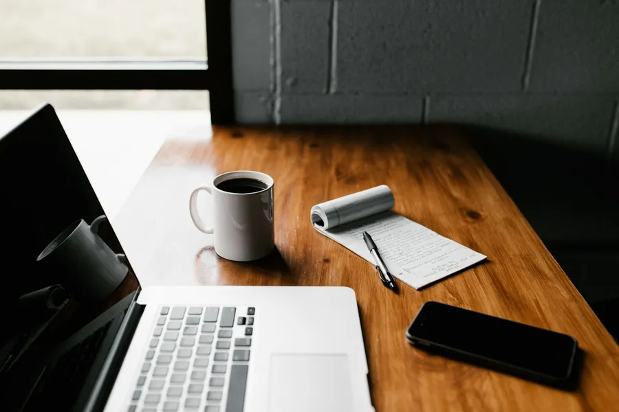 A laptop, coffee and notepad on a wooden desk