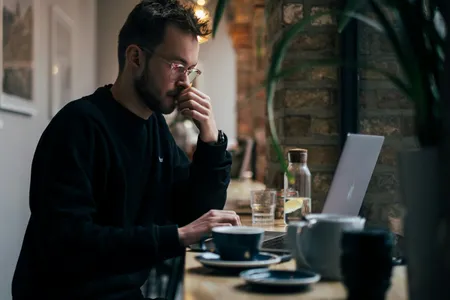 A man thinking while working on a laptop in a cafe