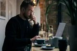 A man thinking while working on a laptop in a cafe