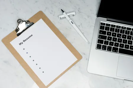 A printed resume on a clipboard next to a laptop and a pen